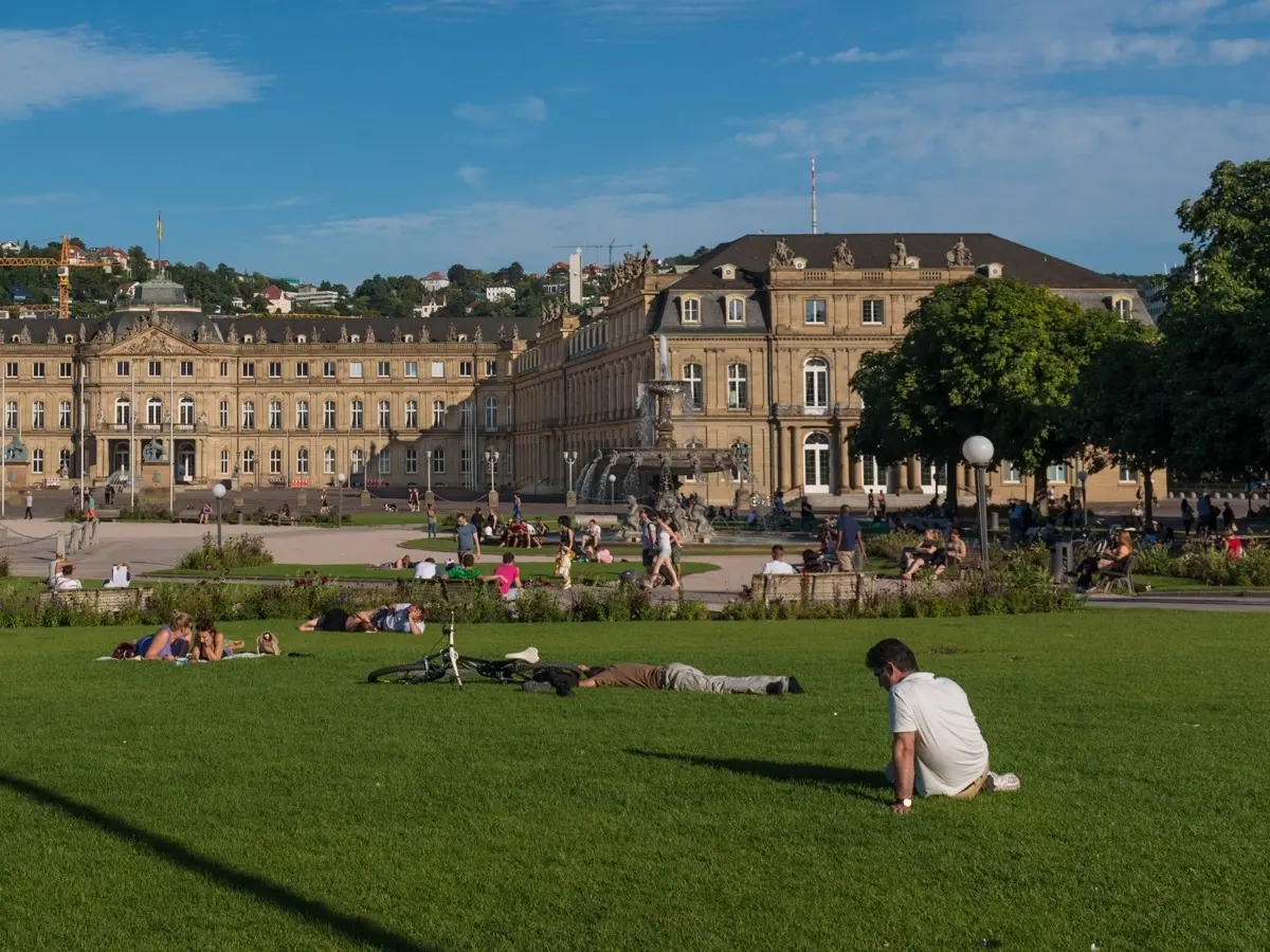 Menschen sitzen einzeln oder in kleinen Gruppen auf der Wiese des Schlossplatzes vorm Neuen Schloss in Stuttgart