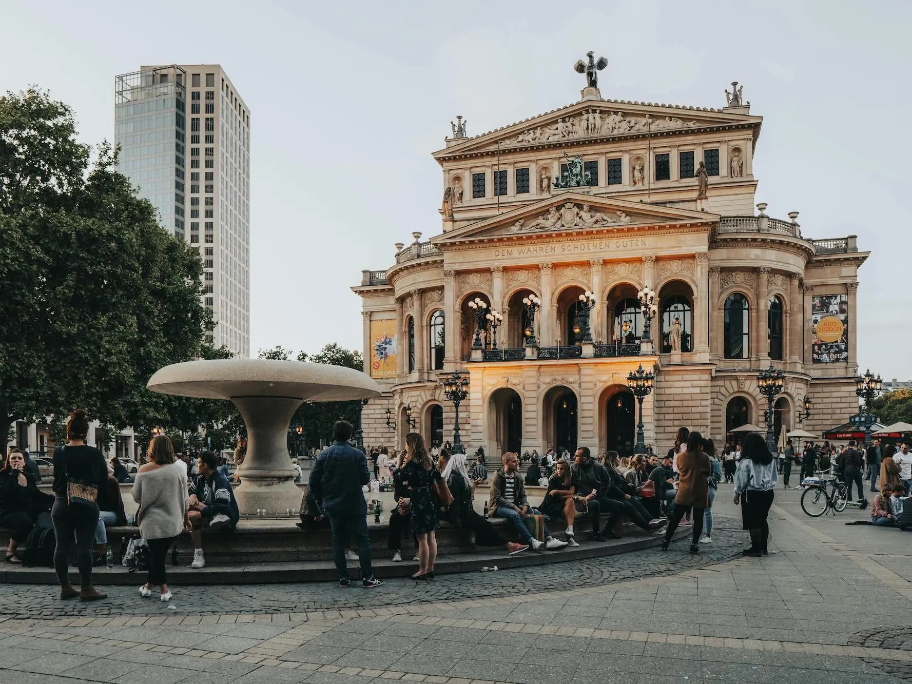 Menschen in Frankfurt am Main sitzen und stehen rund um den Lucas-Brunnen am Frankfurter Opernplatz und unterhalten sich